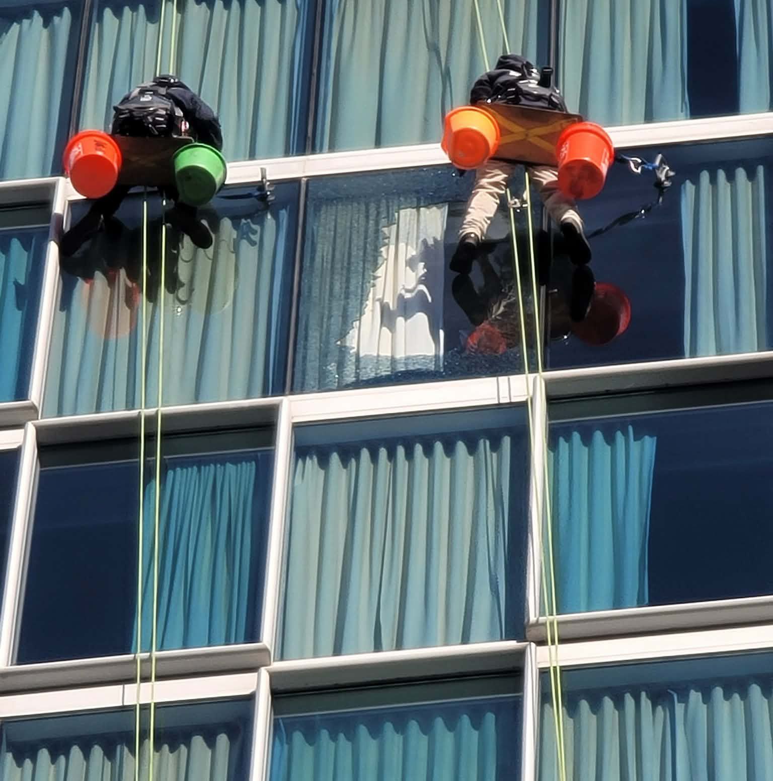 Two window washers suspended from ropes cleaning windows on a high-rise building.