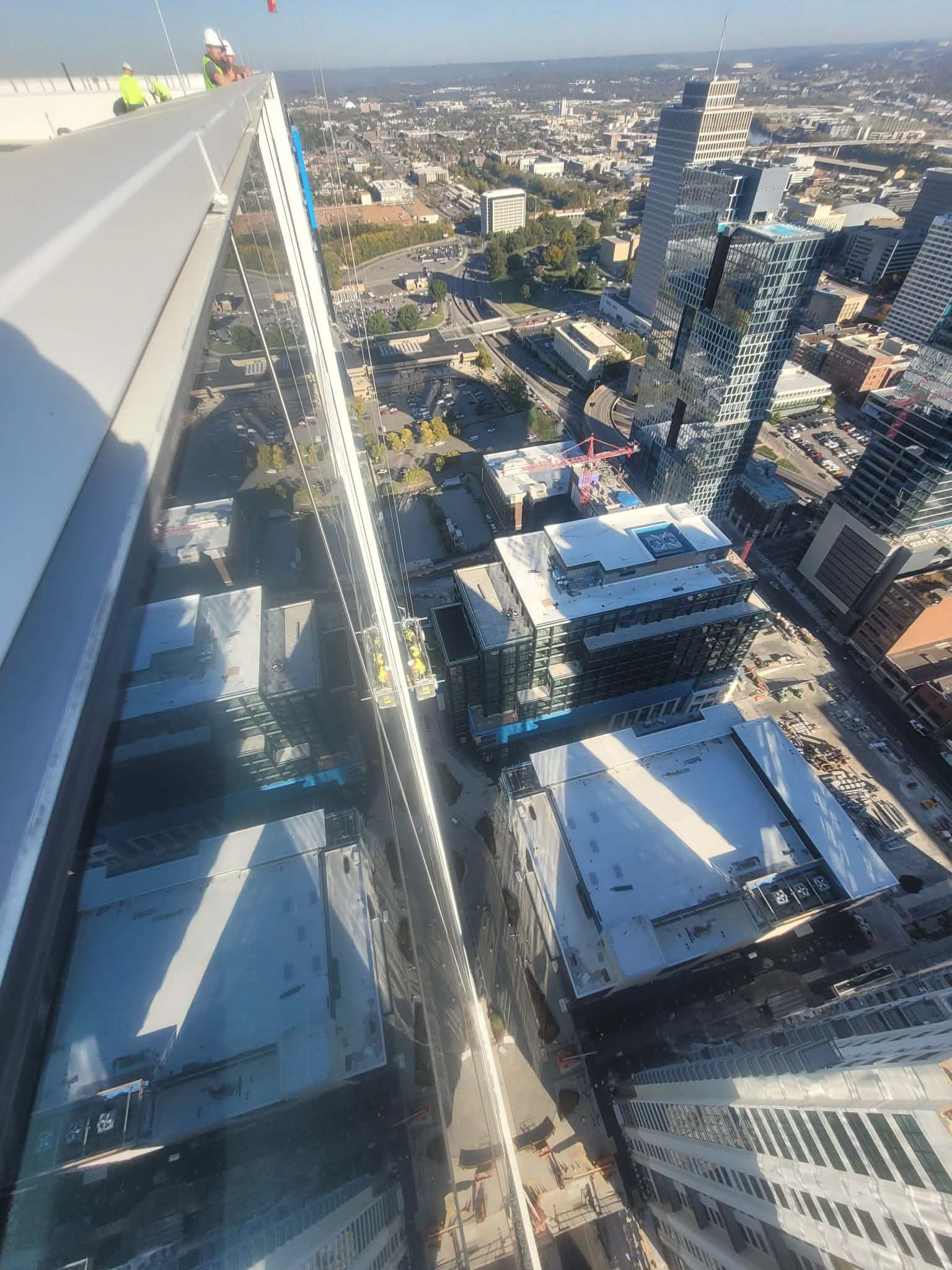 High-angle view of city buildings with glass sides, reflections, and a worker on the edge of a skyscraper.