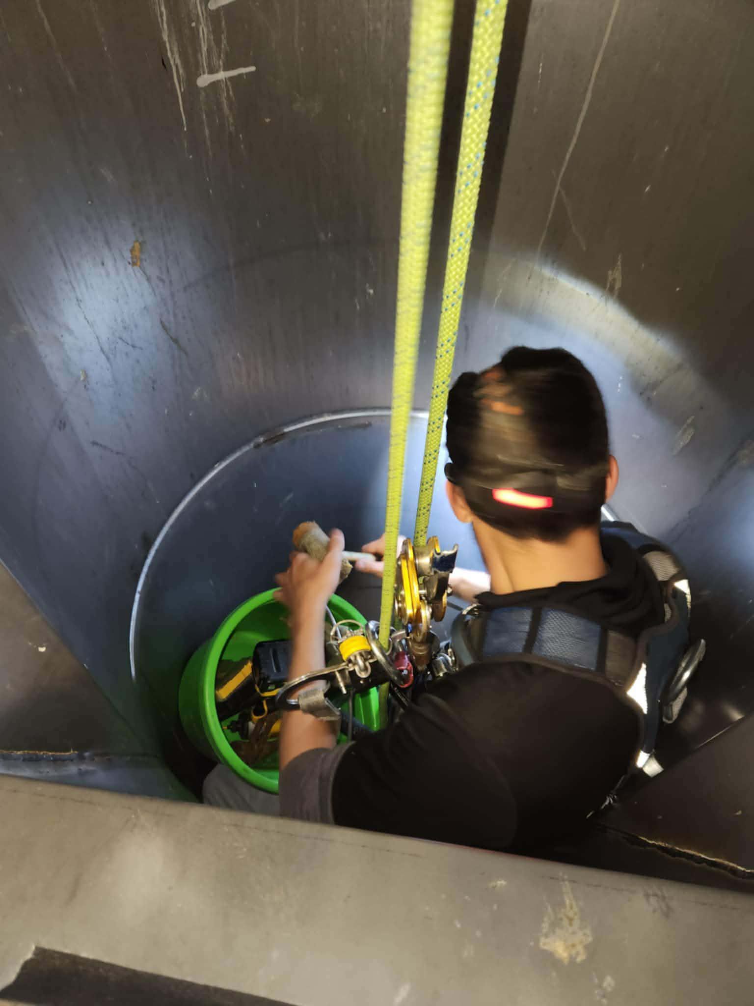 Person inside a cylindrical structure, using ropes and equipment, holding a bucket.