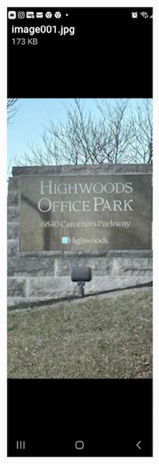 Sign for Highwoods Office Park. The sign is beige with black text. Bare trees in the background.
