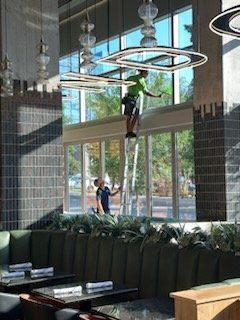 Two people cleaning large windows in a restaurant, one on a ladder.
