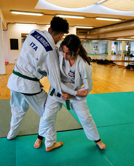 Due artisti marziali si esercitano in una tecnica di presa su un tatami in un dojo.