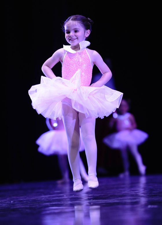 Giovane ballerina con un tutù rosa che si esibisce sul palco con un sorriso, sotto luci viola