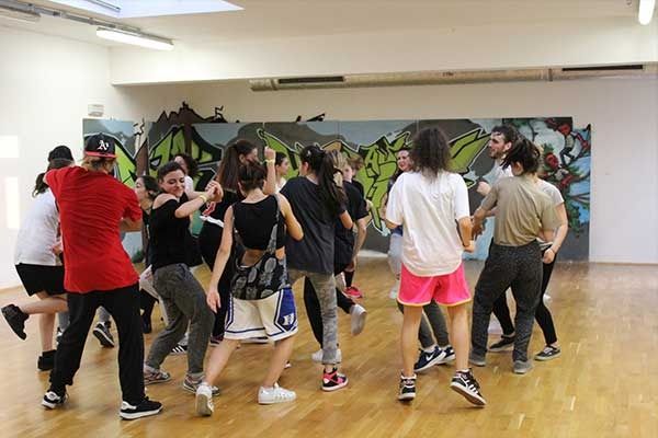 Gruppo di ballerini che si esercitano in uno studio con una parete decorata da un murale colorato.