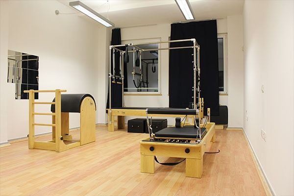 Studio di Pilates con macchine reformer, attrezzature in legno e specchi su un pavimento in legno chiaro.