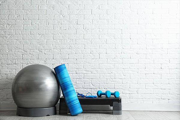 Palle da ginnastica e rulli di schiuma su un tappetino appoggiato a un muro di mattoni bianchi.