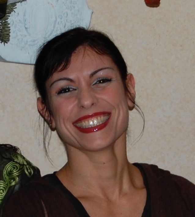Donna sorridente con capelli scuri e rossetto rosso davanti a una parete chiara
