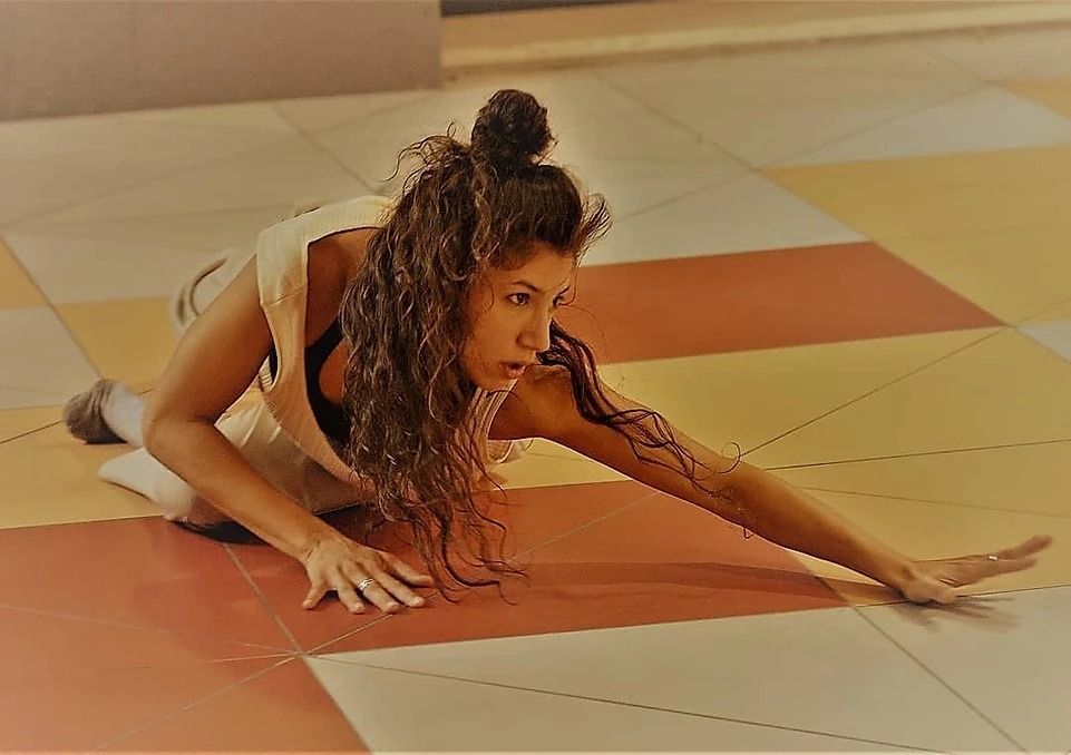 Una persona striscia a terra su un pavimento piastrellato in una posa di danza, allungando un braccio in avanti.