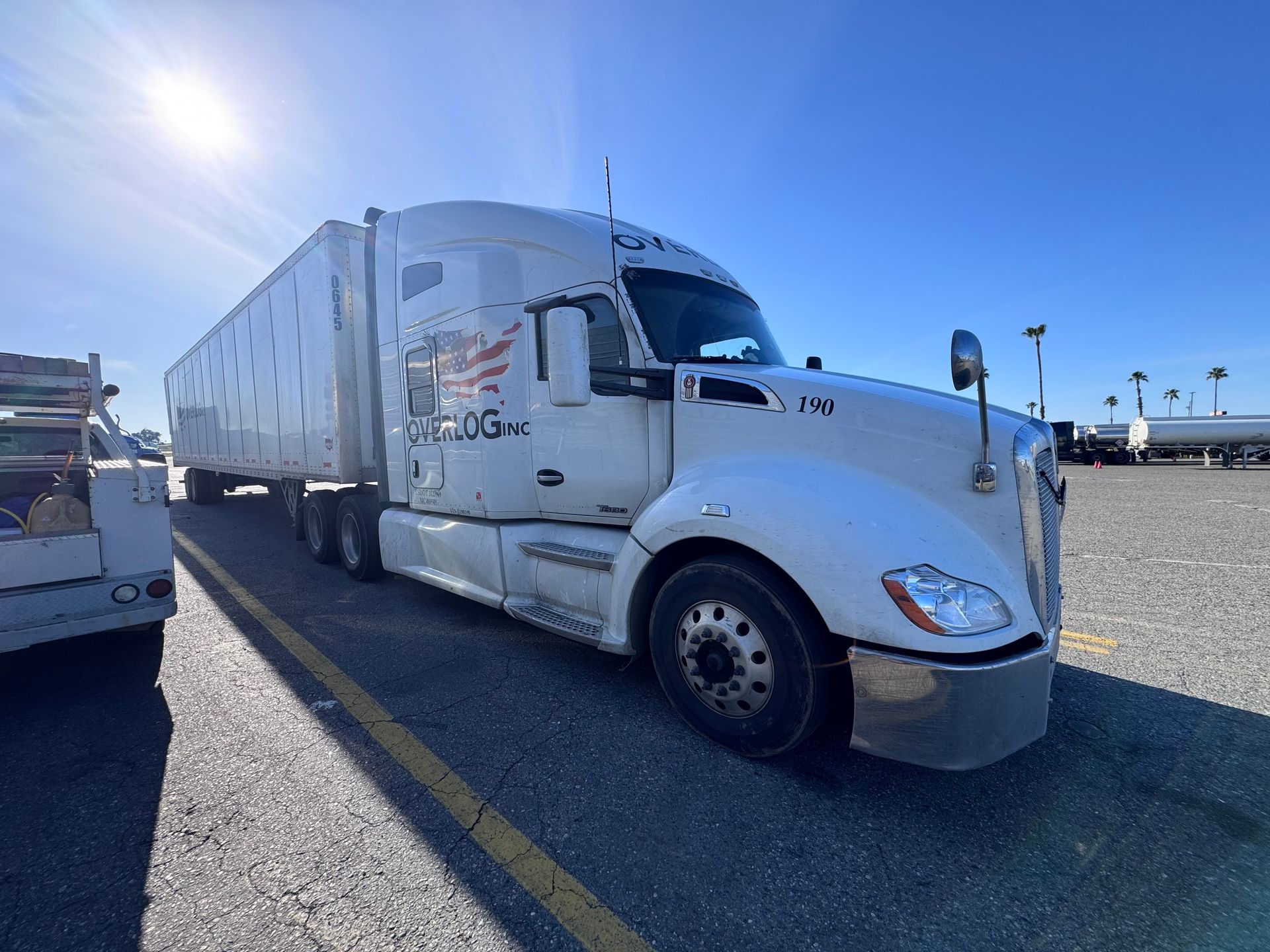 White semi-truck parked outdoors on a sunny day. The truck has a trailer and company logos on the cab.