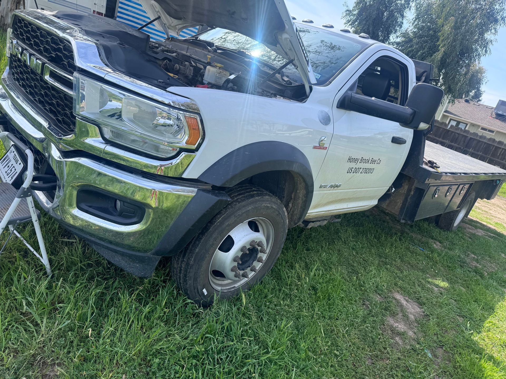 White Ram 5500 flatbed truck with hood open, parked on grass in a yard.
