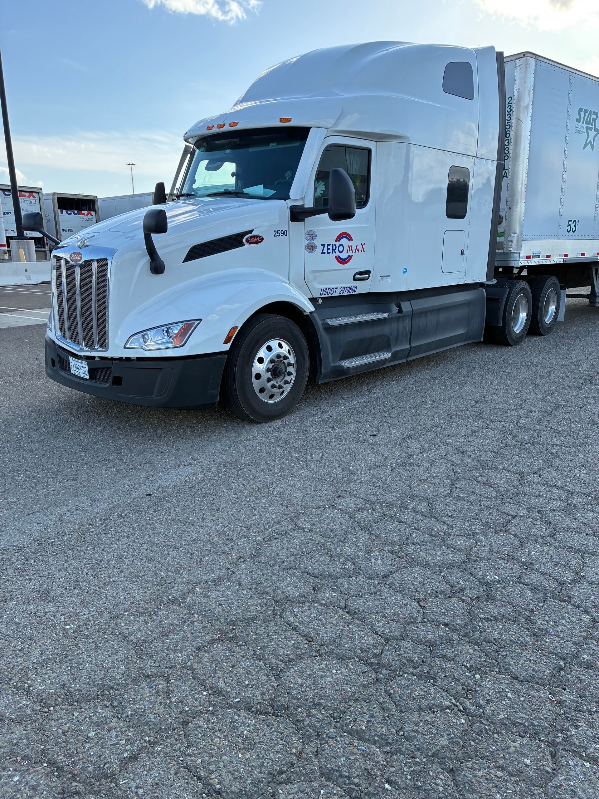 White semi-truck with a trailer parked on gravel. Blue sky background.