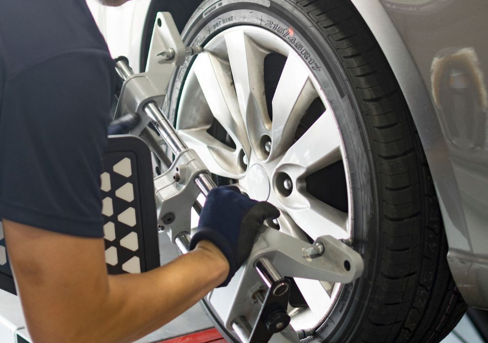 Mechanic in gloves clamping wheel alignment equipment to a car’s alloy wheel