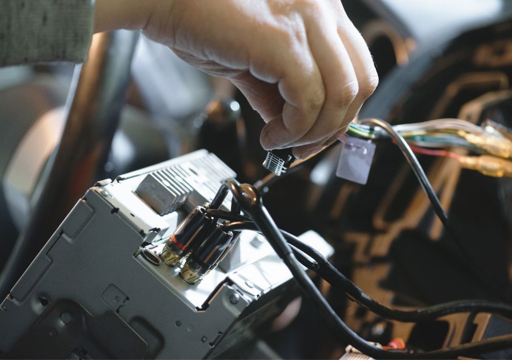 Hand plugging a wiring connector into the back of a car stereo