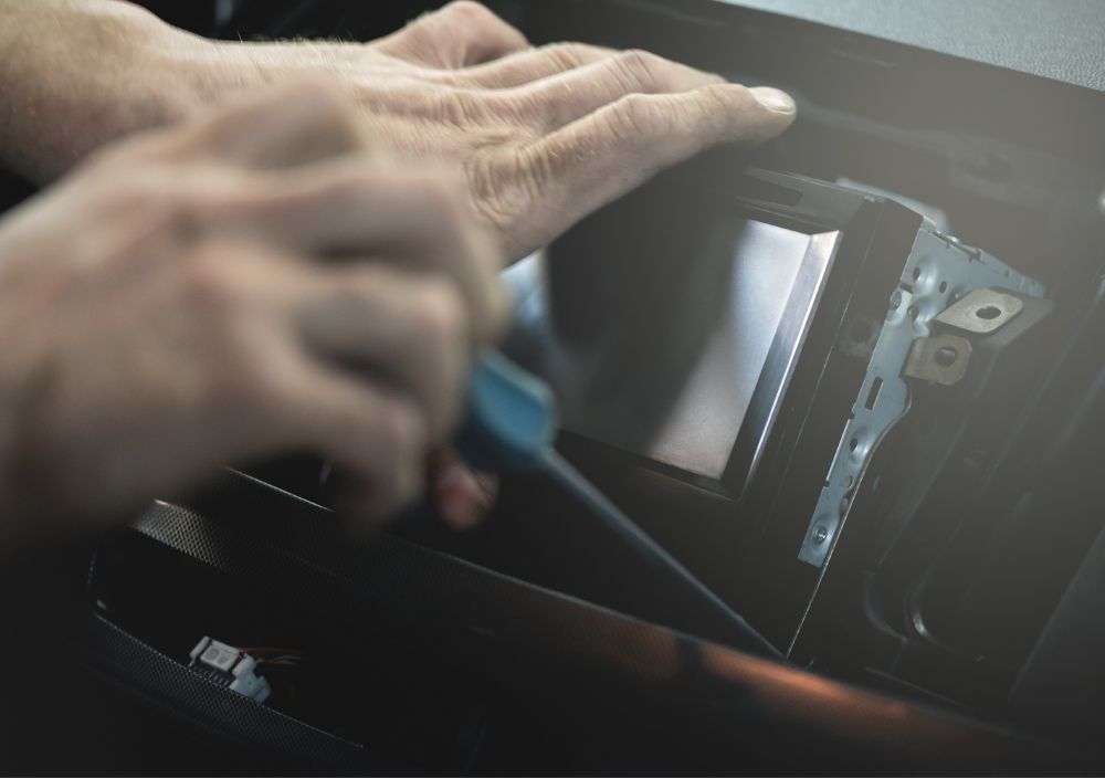 Hands fitting a new touchscreen stereo into a car dashboard