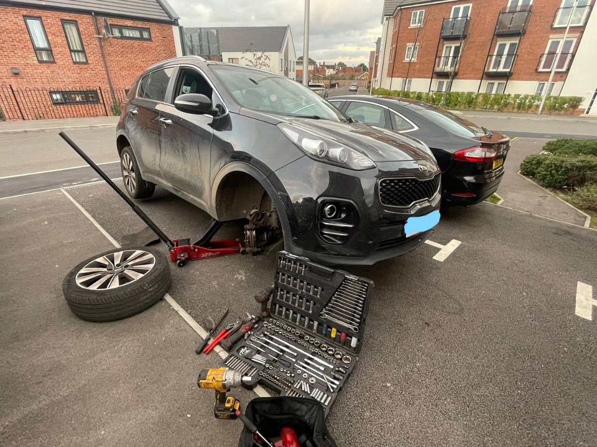Kia Sportage on a jack in a residential car park with its front wheel off for a brake pad replacement in Shinfield