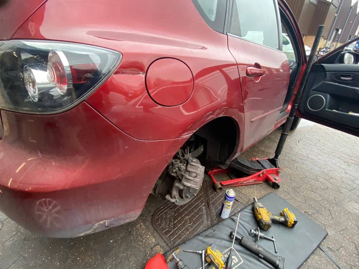 Red Mazda raised on a trolley jack with a rear wheel off and tools laid out on a mat