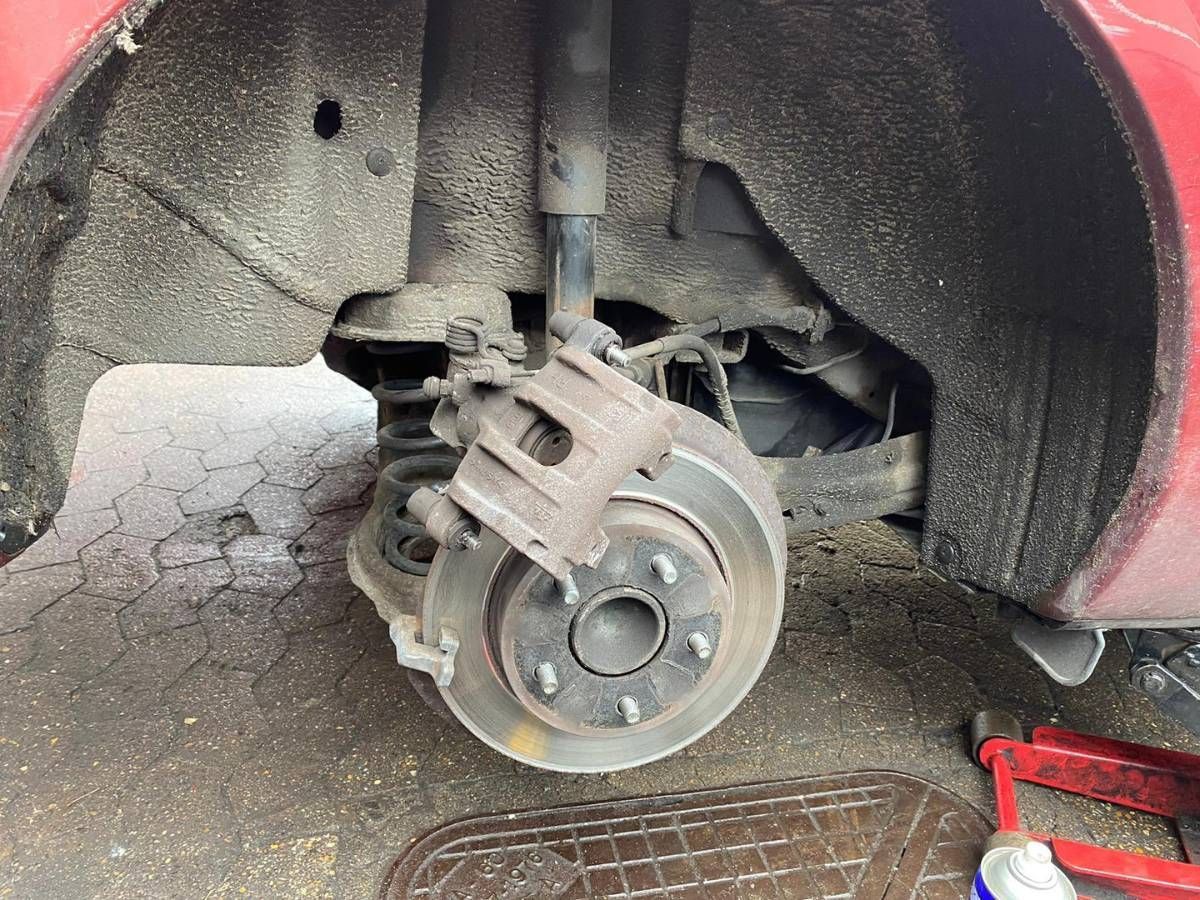 Rear brake disc and caliper carrier on a red Mazda with the wheel removed