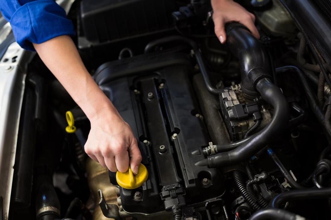 Mechanic’s hand on the yellow oil filler cap of a car engine