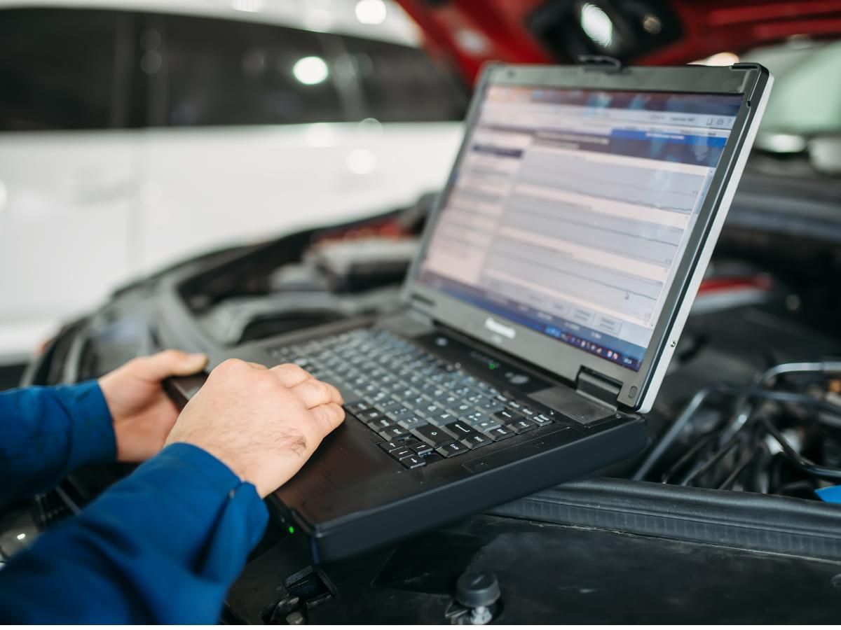 Mechanic running diagnostics on a laptop under an open bonnet