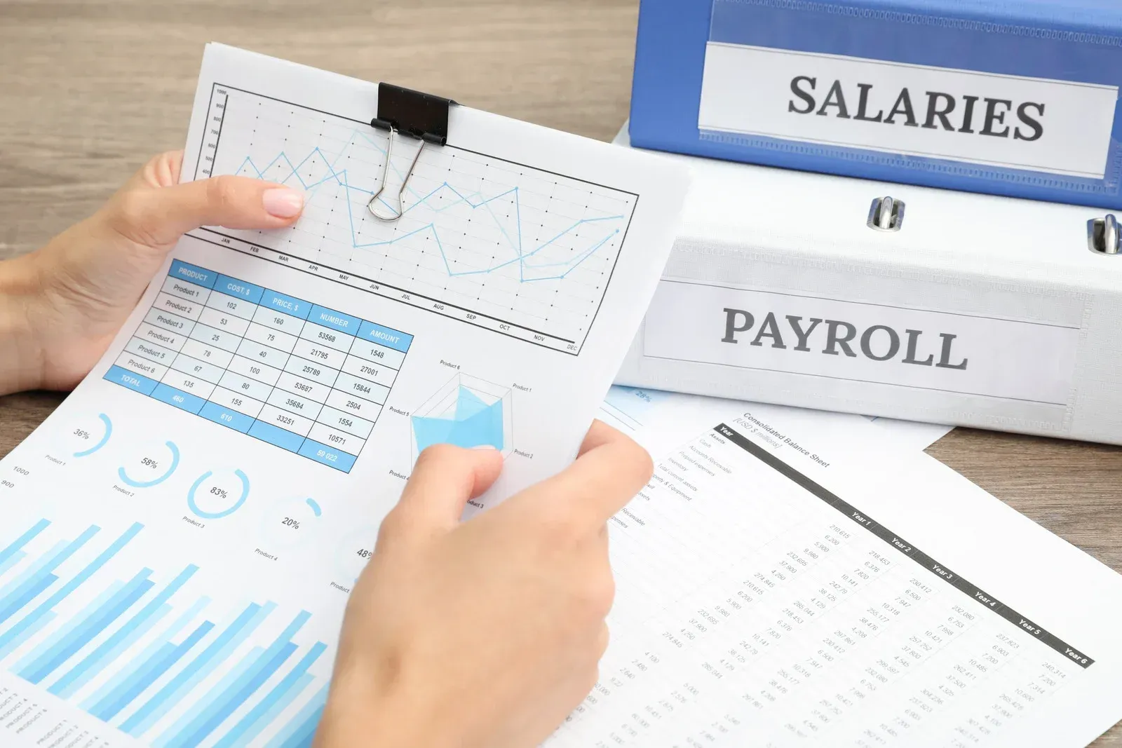 Hands reviewing salary and payroll documents with charts on a desk.