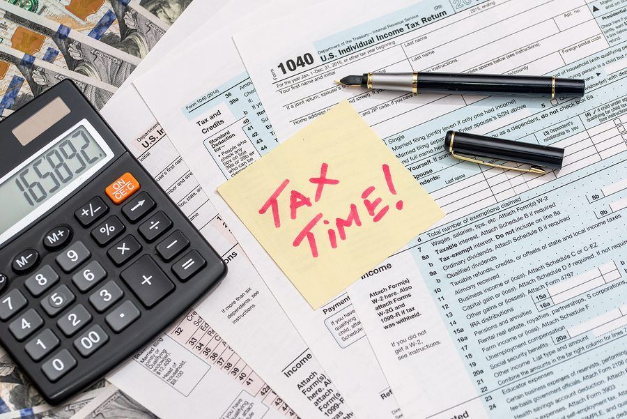 Calculator, tax forms, pen, and sticky note reading “TAX TIME!” on a desk