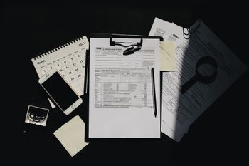 Desk with scattered papers, notebook, calculator, smartphone, and keys on a dark background
