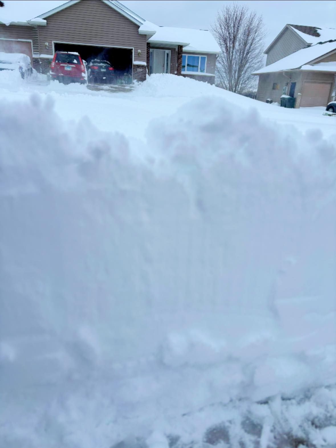 Tall snowbank in front of a suburban house and driveway after heavy snowfall