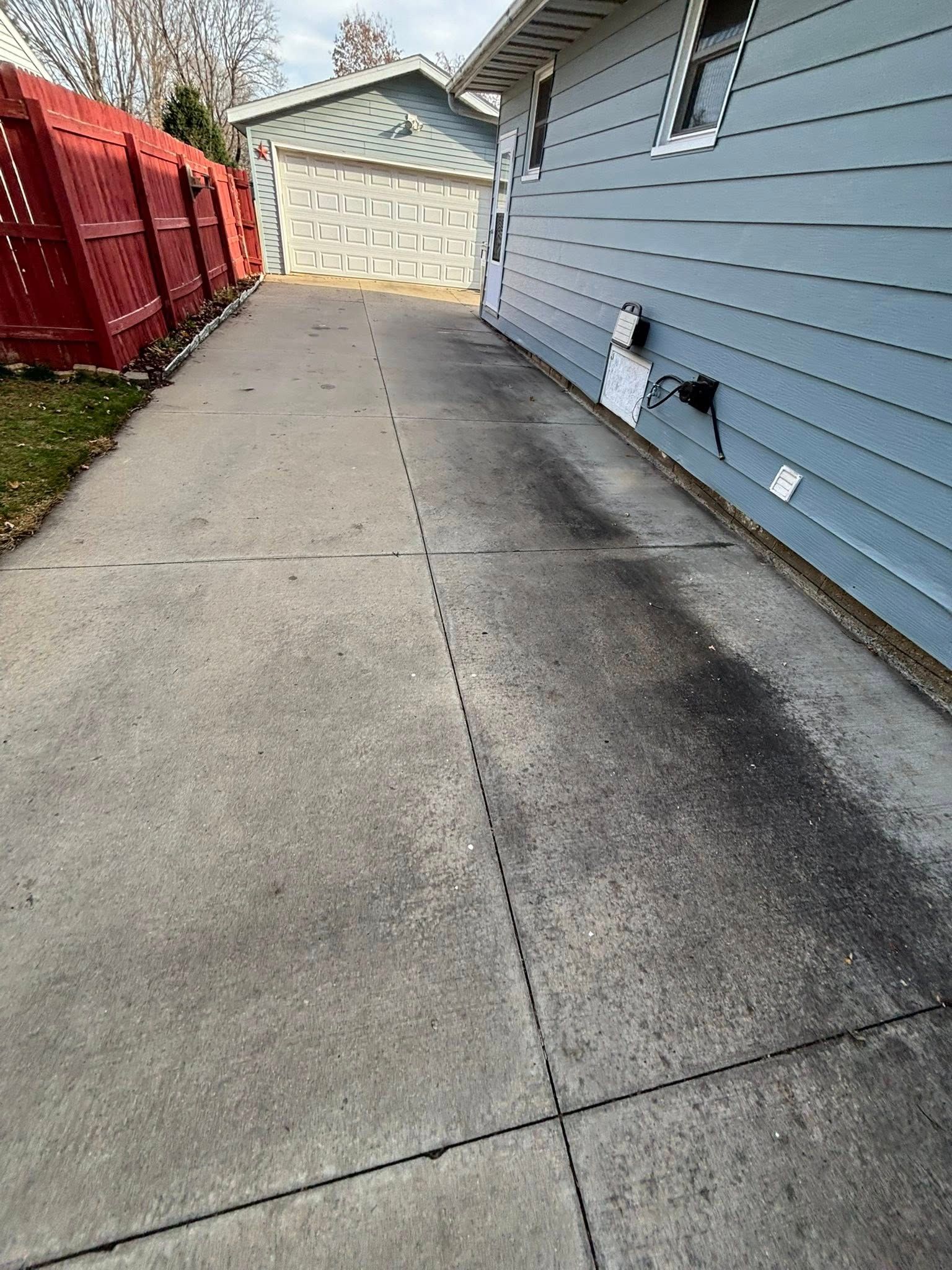 Long concrete driveway beside a blue house, leading to a garage with red fencing on the left.