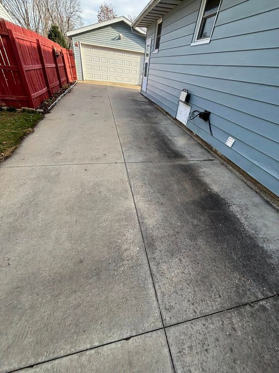 Long concrete driveway beside a blue house, leading to a garage with red fencing on the left.