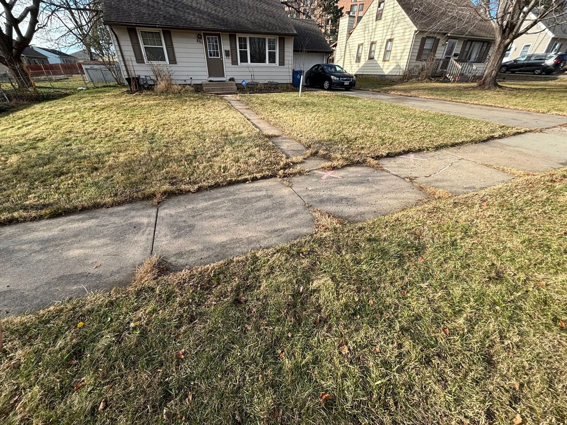 Suburban house with bare lawns and a cracked sidewalk in the foreground