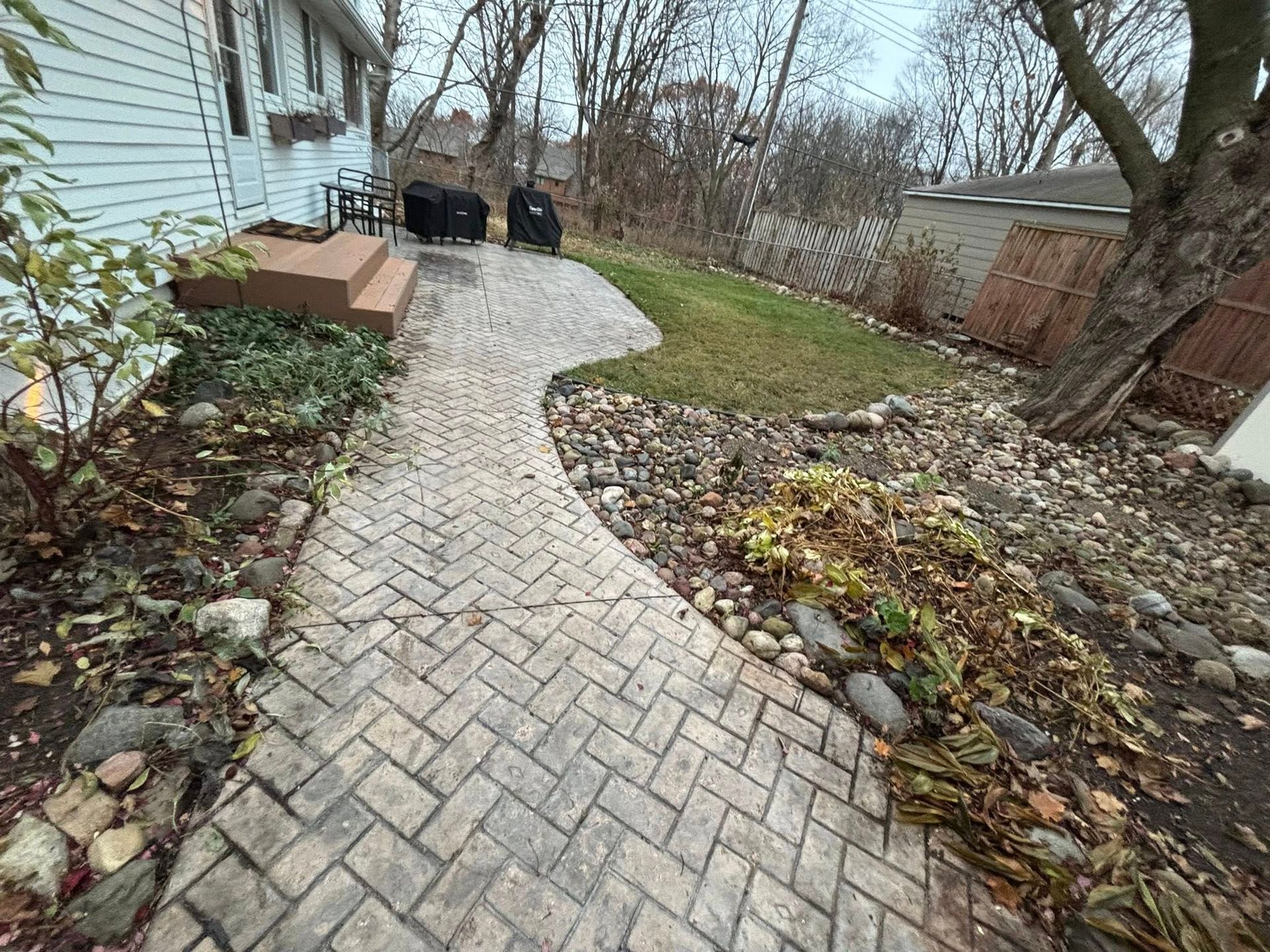 Brick walkway curving past a house toward a yard, with two people sitting near the far end.
