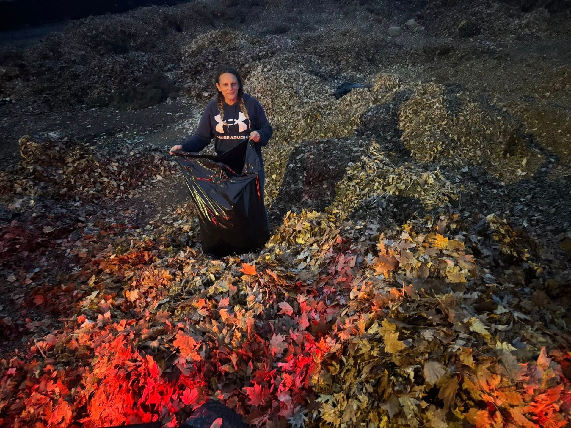 Person standing among dark rocks and bright red-orange seaweed, holding a black bag.