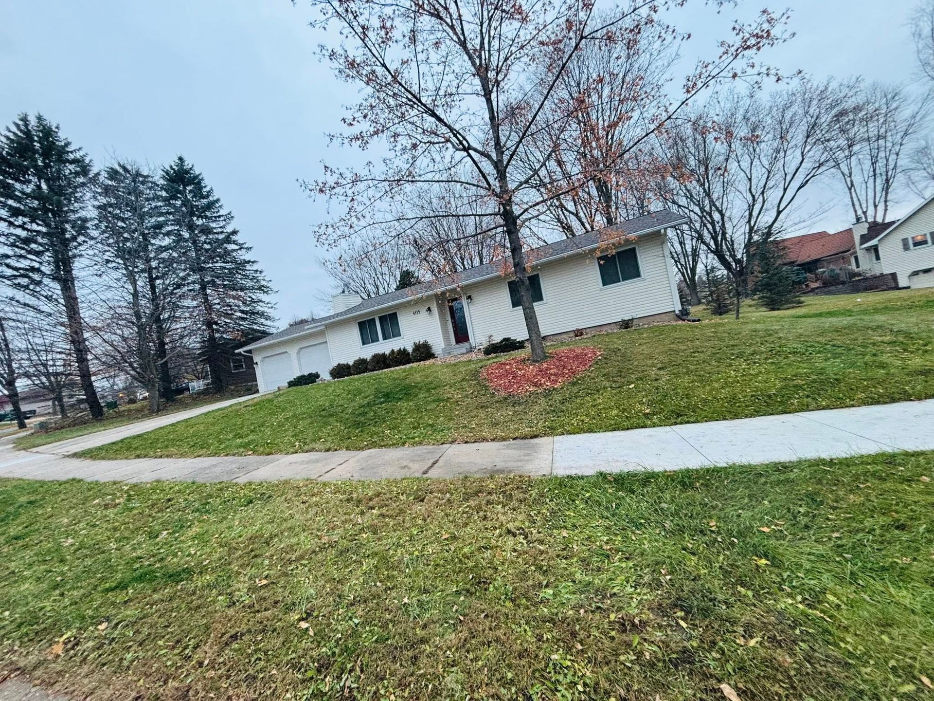 Tilted view of a white house with bare trees, green lawn, and a sidewalk on an overcast day