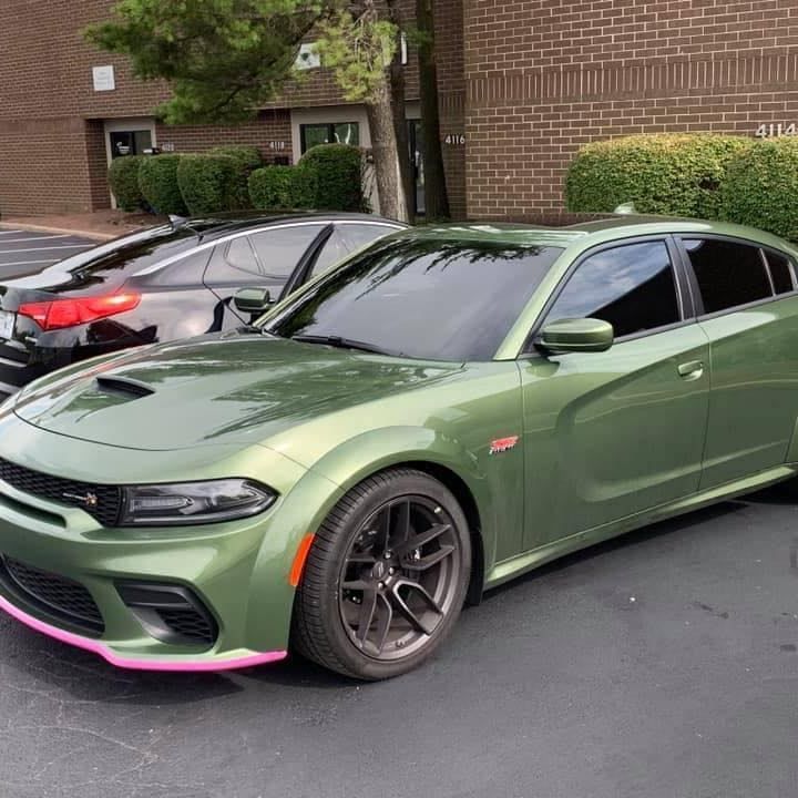 A green dodge charger is parked in front of a brick building.