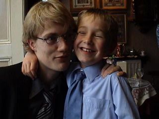 A young boy grins as he curls his arm around the shoulders of a young man. Both are dressed in shirts and ties which match the formal but comfortable restaurant surrounds.