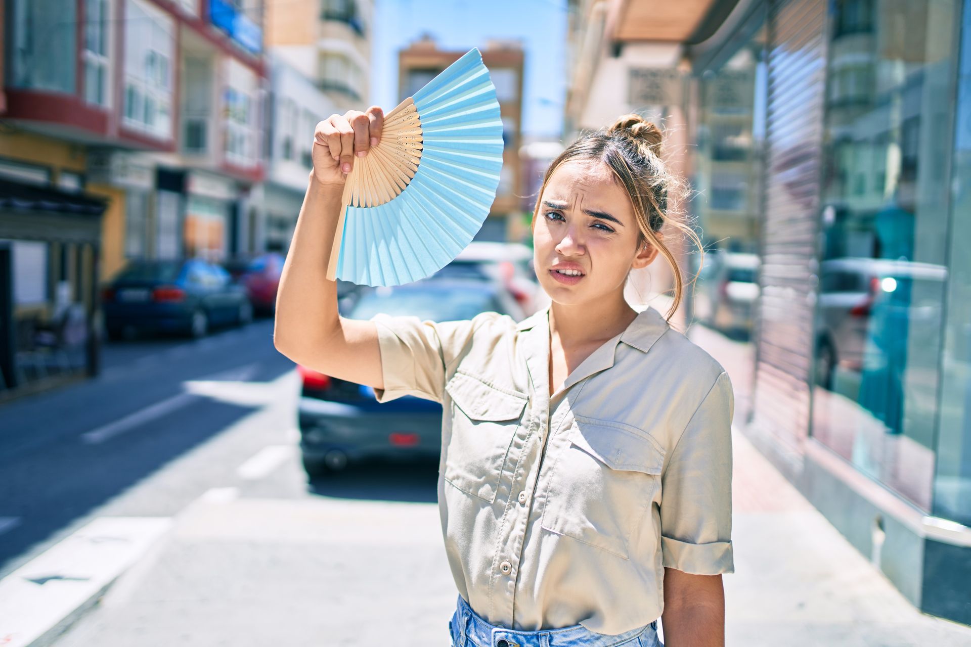 A young woman scrunches her face up in discomfort as she fans herself in an attempt to cool down in a hot city.