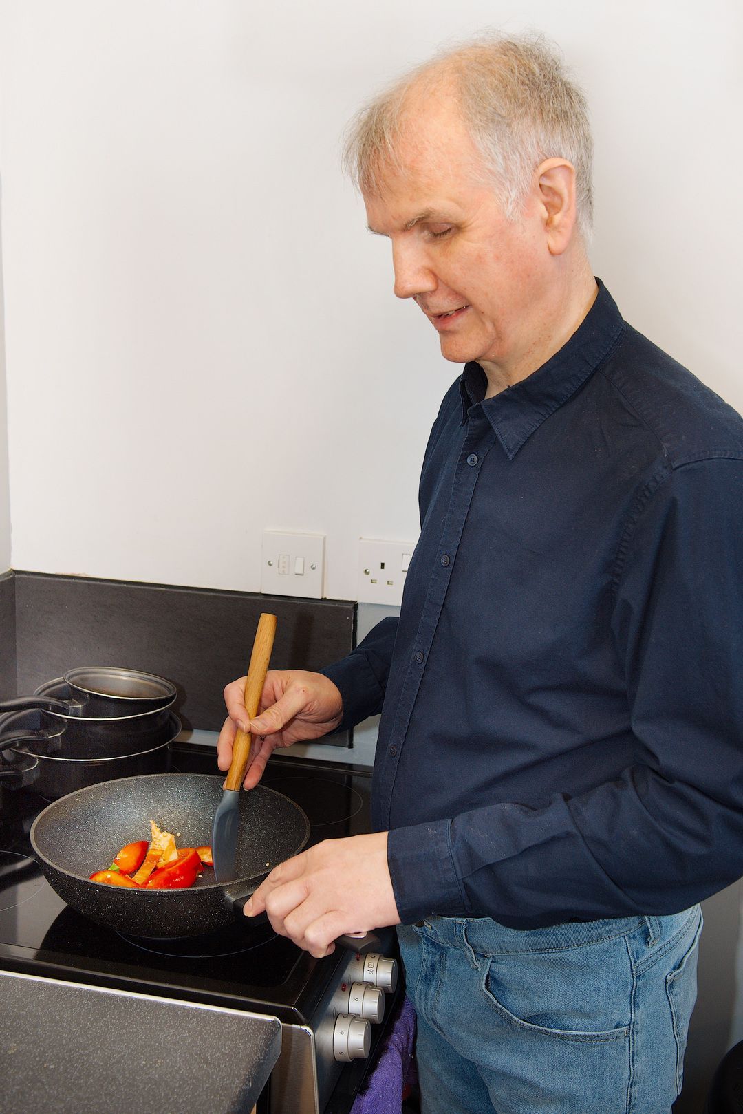 Philip Anderson stands next to a hob, stirring food in a pan as it cooks.