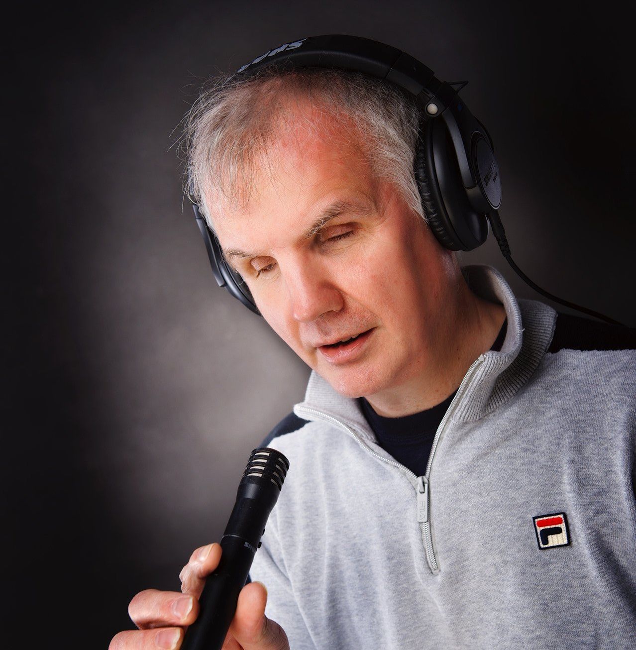 Philip Anderson leans forwards towards a microphone as he speaks into it.