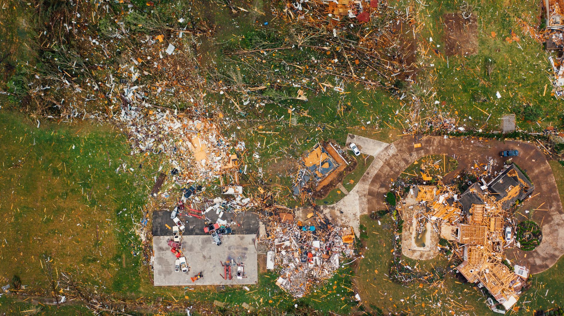 A wooden house has been shredded by an extreme weather event, its timbers strewn across the landscape with abandoned cars.