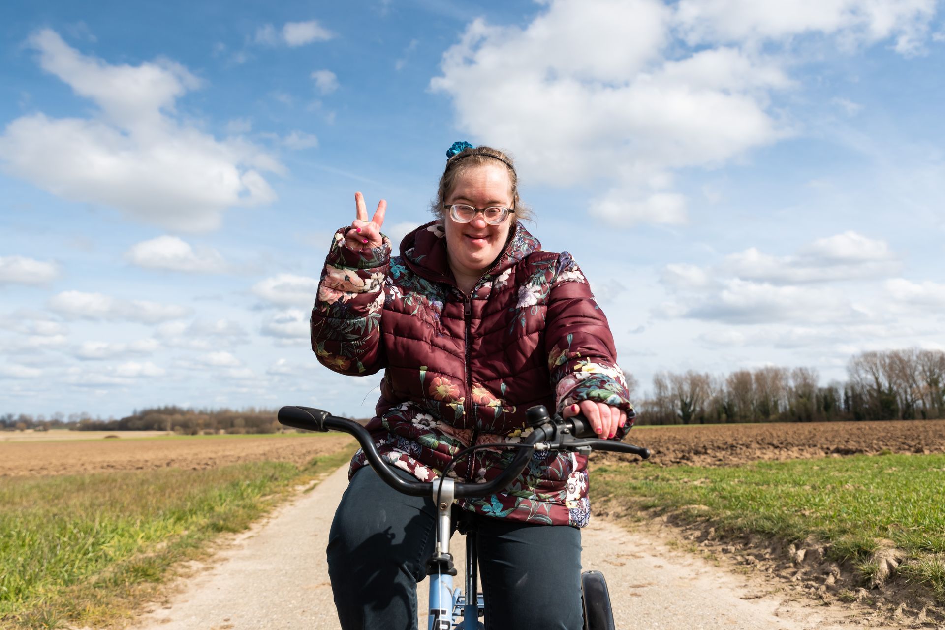 A young woman with Down Syndrome smiles as she rides her bike through some fields.