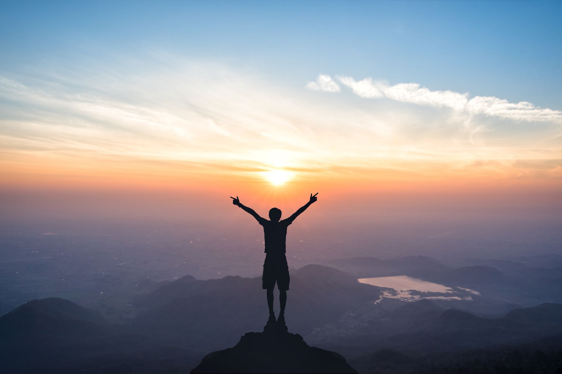 Silhouetted figure standing, arms spread, atop a mountain