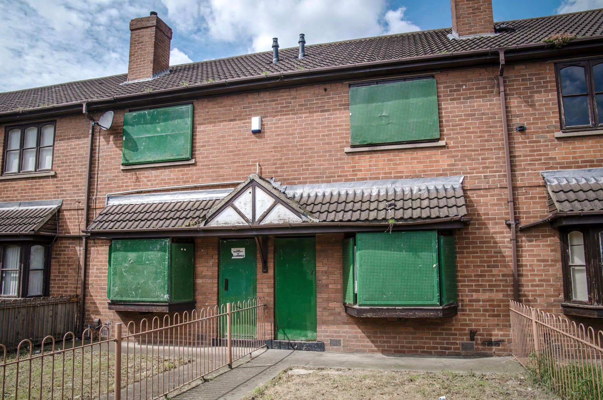 Photograph of a terrace of run down houses with windows boarded up.