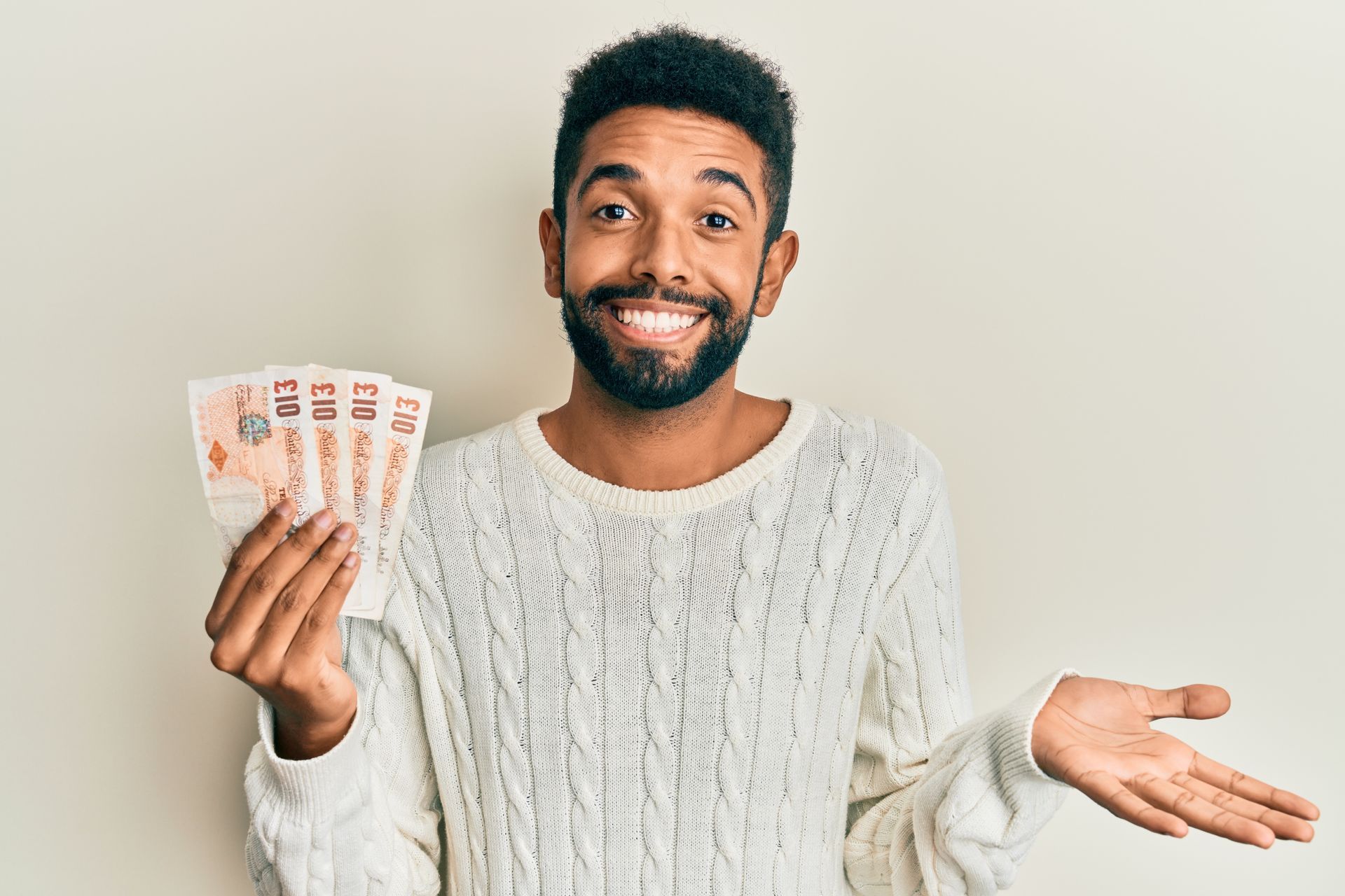 Photo of a young man smiling while holding four ten pound banknotes.