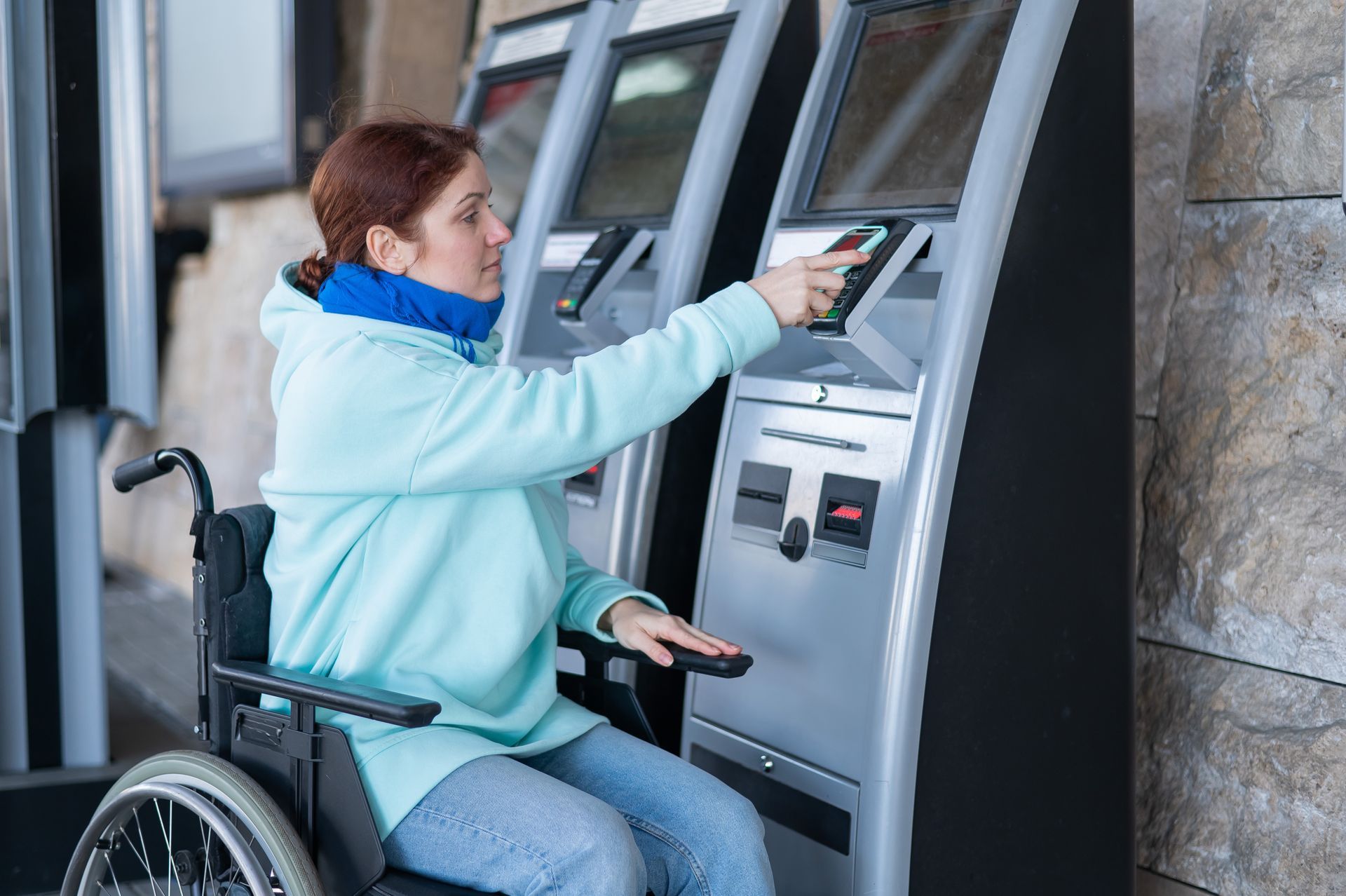 A woman in a wheelchair pays for train tickets at a digital kiosk which stands too high for wheelchair users.