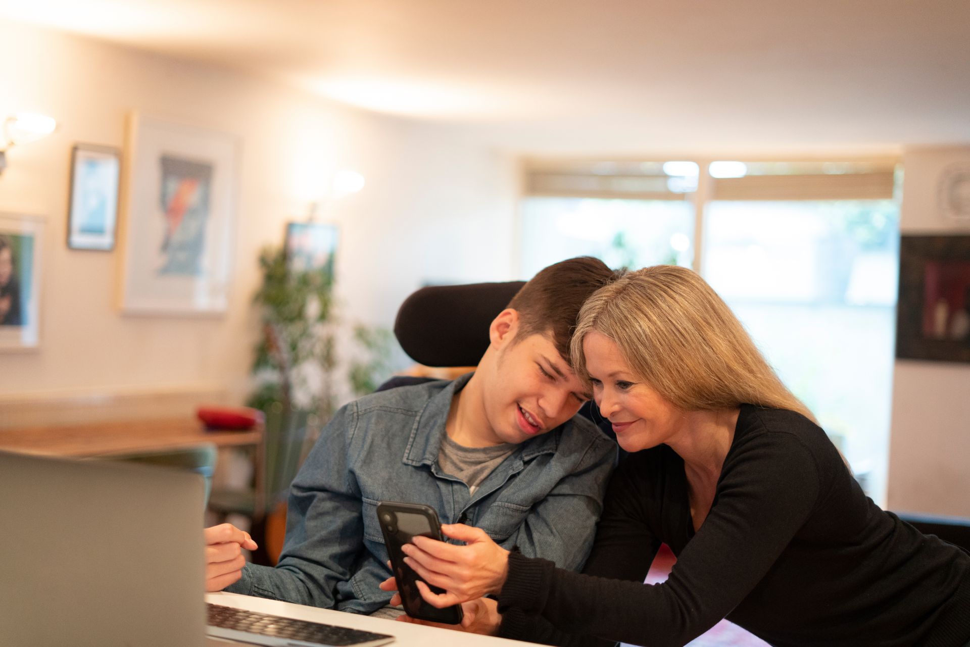 A teenager with severe learning disabilities looks at his phone with his mother.