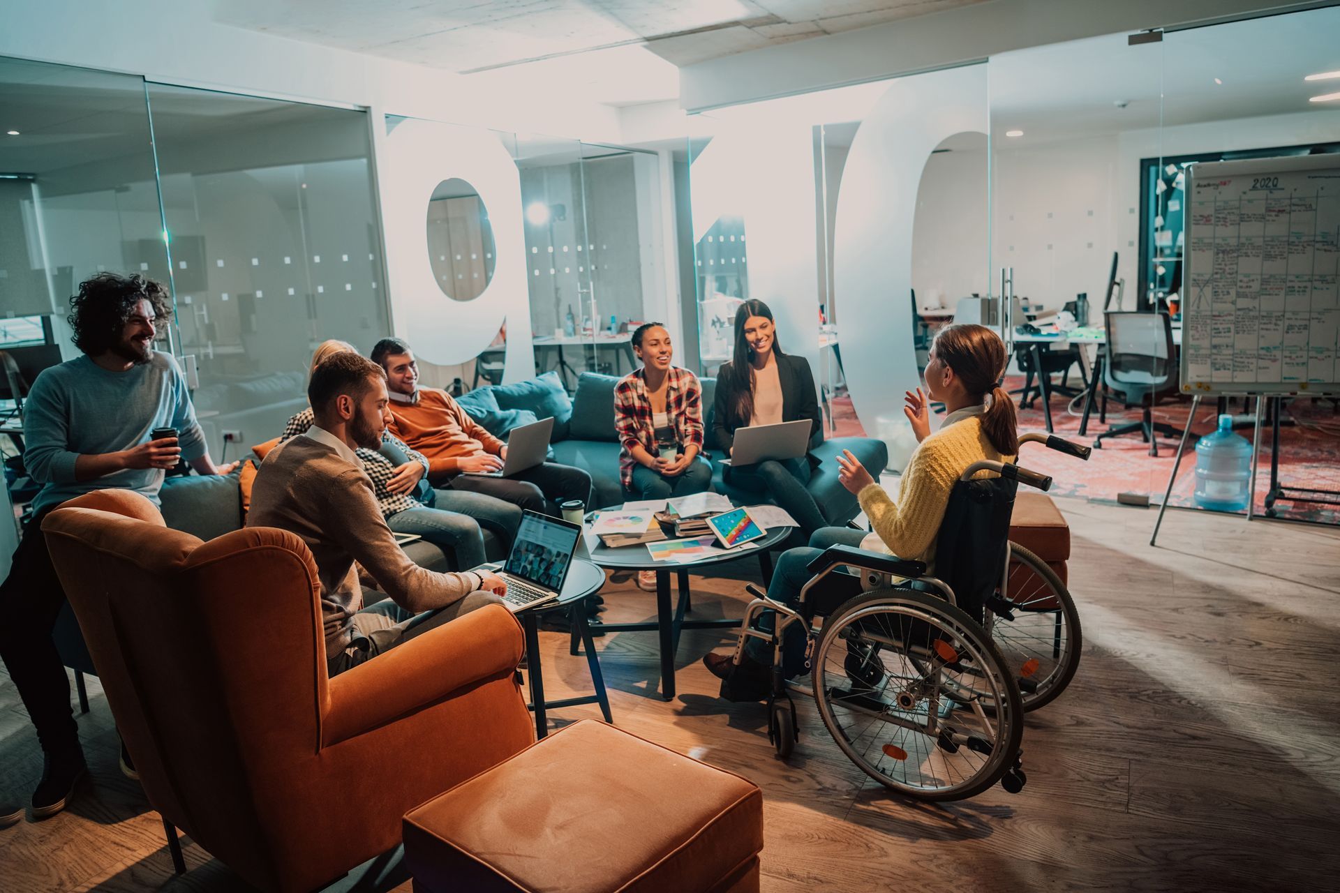 A woman who uses wheelchair attends a workshop in a modern office, alongside a group of young people.
