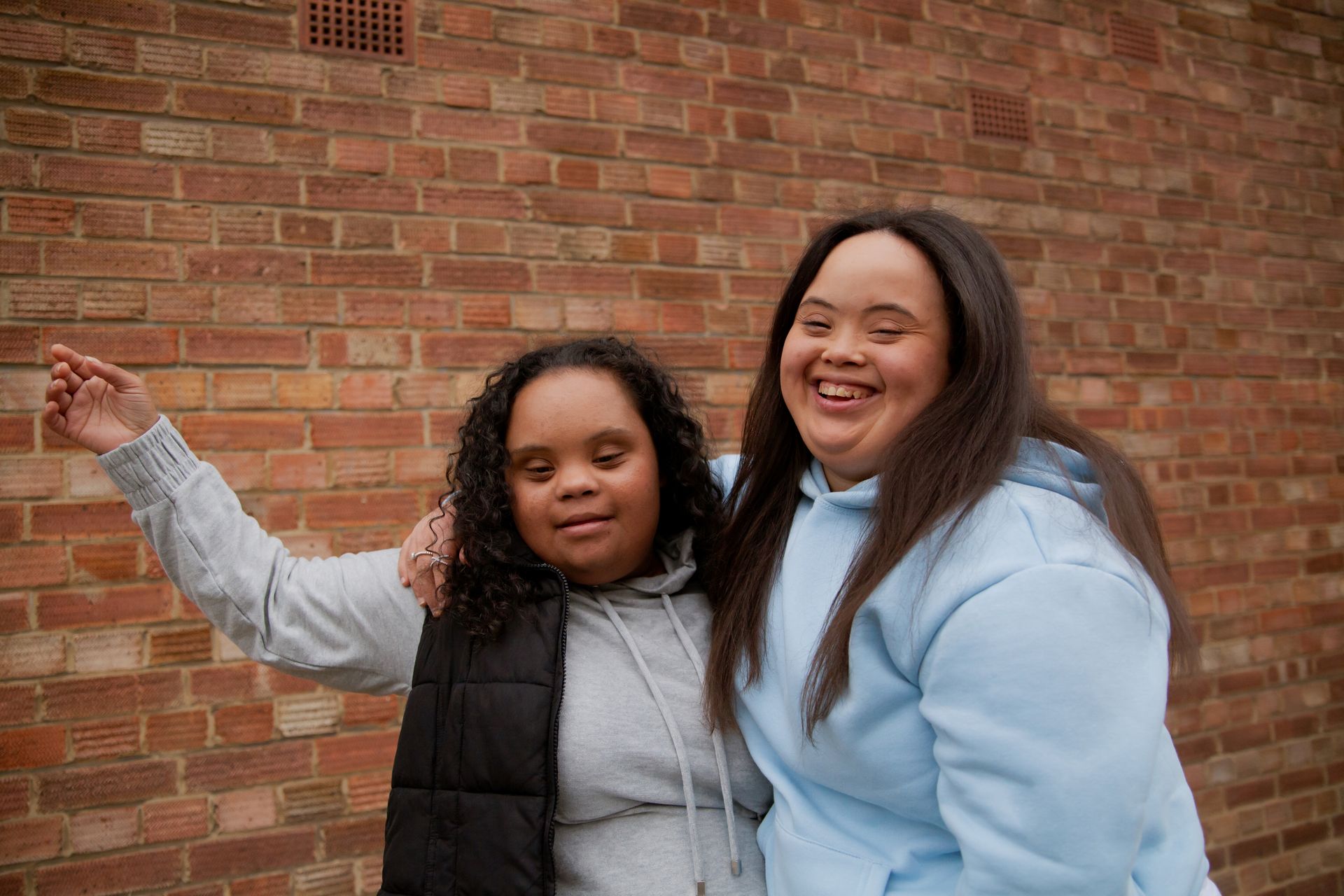 Two female friends with Down Syndrome in casual wear beam and laugh as they hug each other.