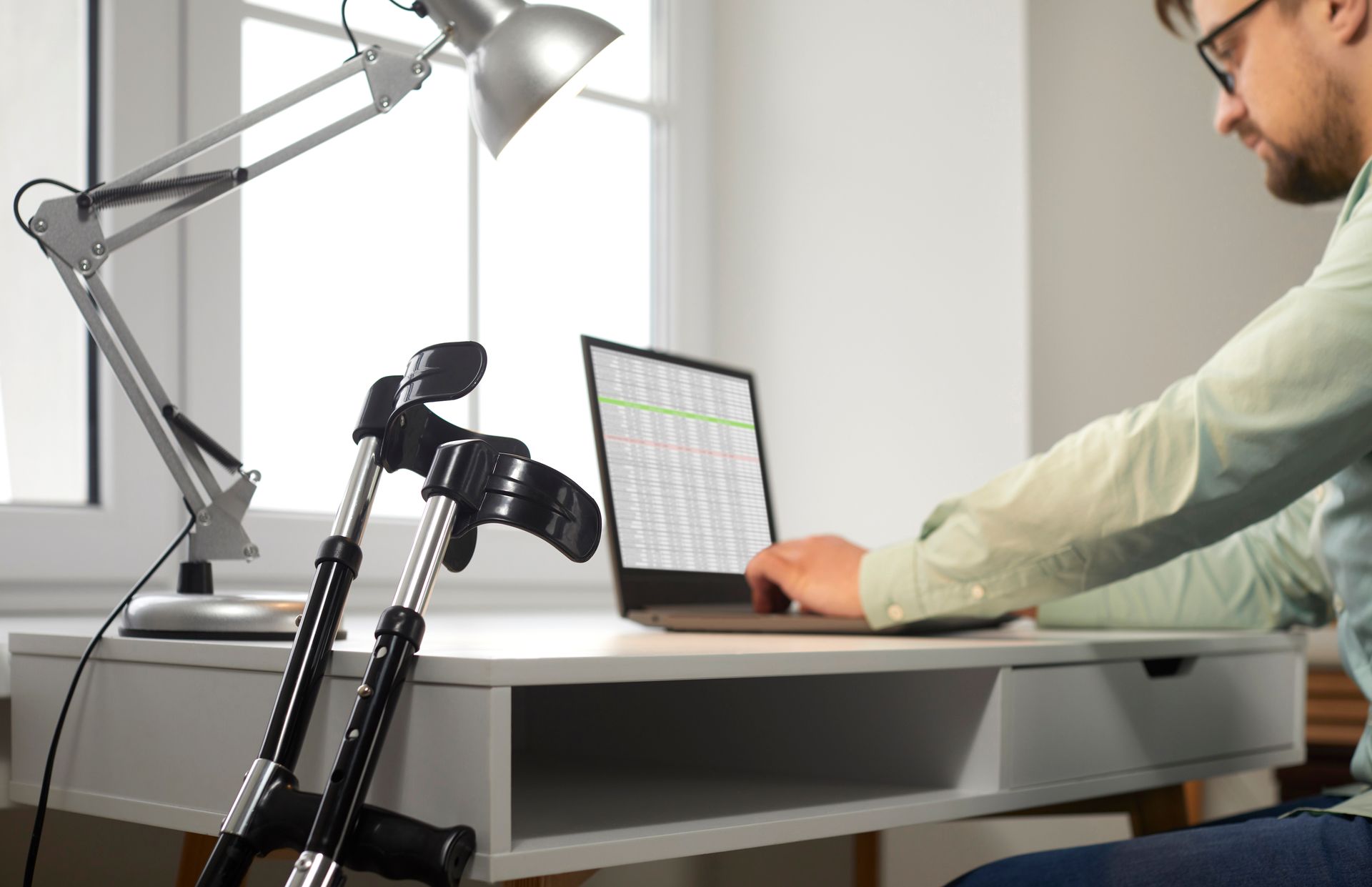 Photograph of a man searching through job listings on a laptop, with a pair of walking aids leaning against the desk.