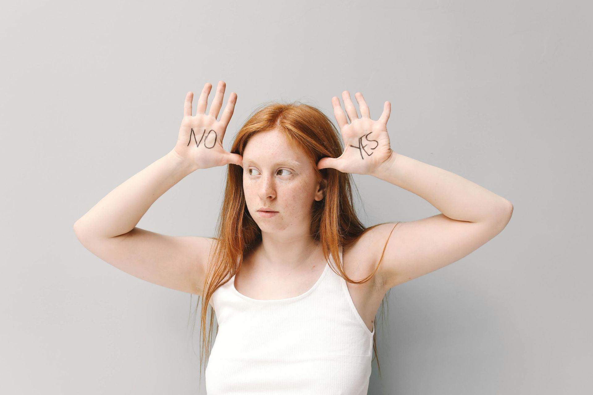 A woman in a white tank top holds a 'yes' and 'no' on her hands, symbolizing indecision. 