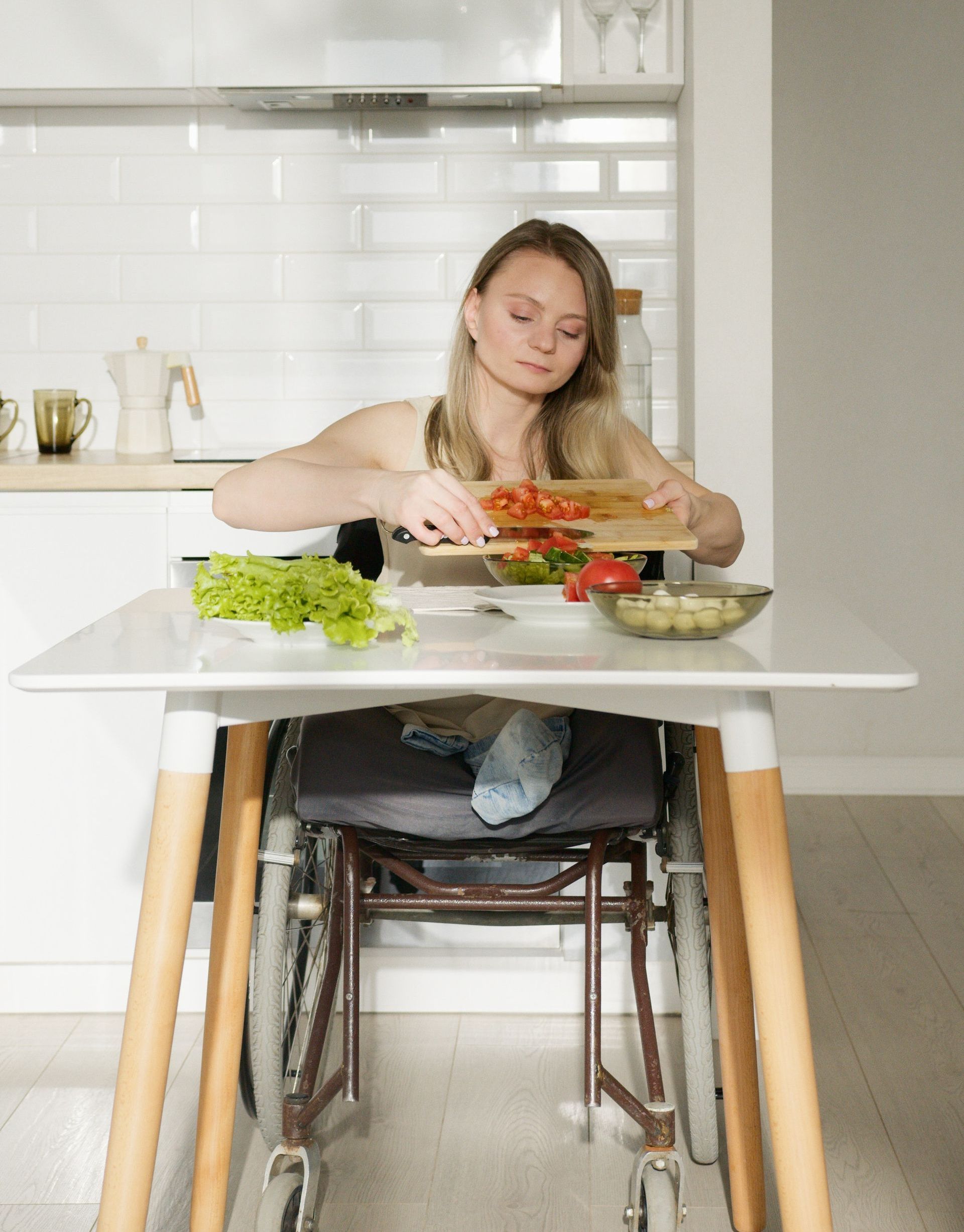 A young woman with sight loss and lower limb disabilities chops tomatoes in a neat kitchen.